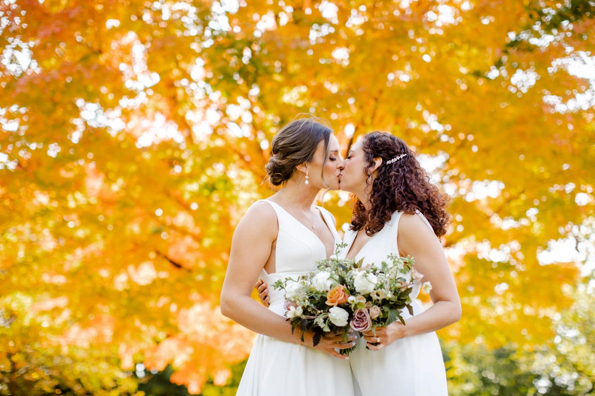 Newlyweds Kate Bolig and Joslyn DeSantis steal a kiss in front of a gorgeous, blooming fall tree.